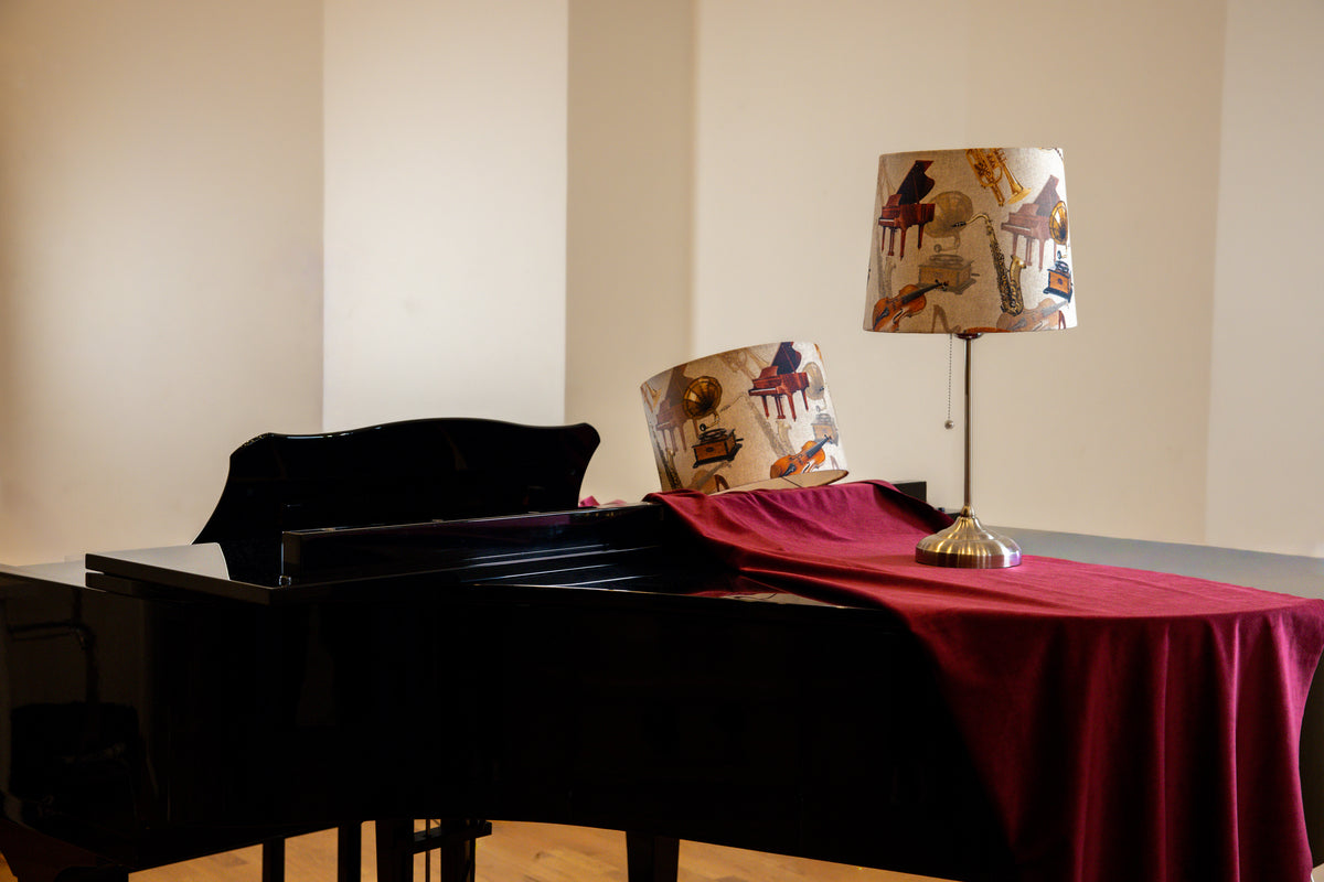 Piano with a red cover and a lamp on a stand against a beige wall.